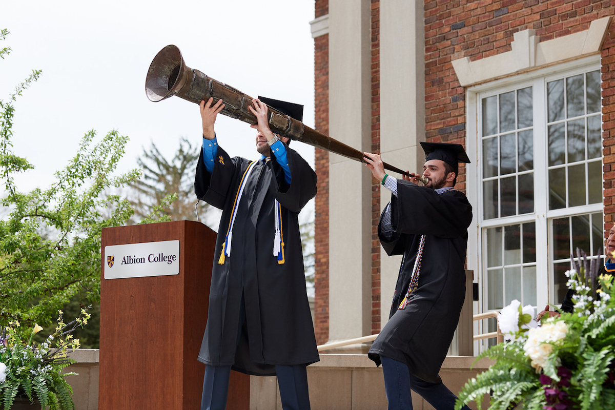 Two students at graduation blowing the senior horn at commencement.